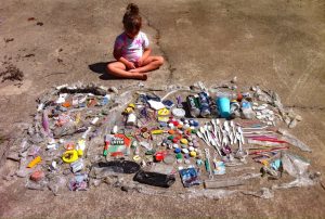 Child sitting with trash collected on a beach.