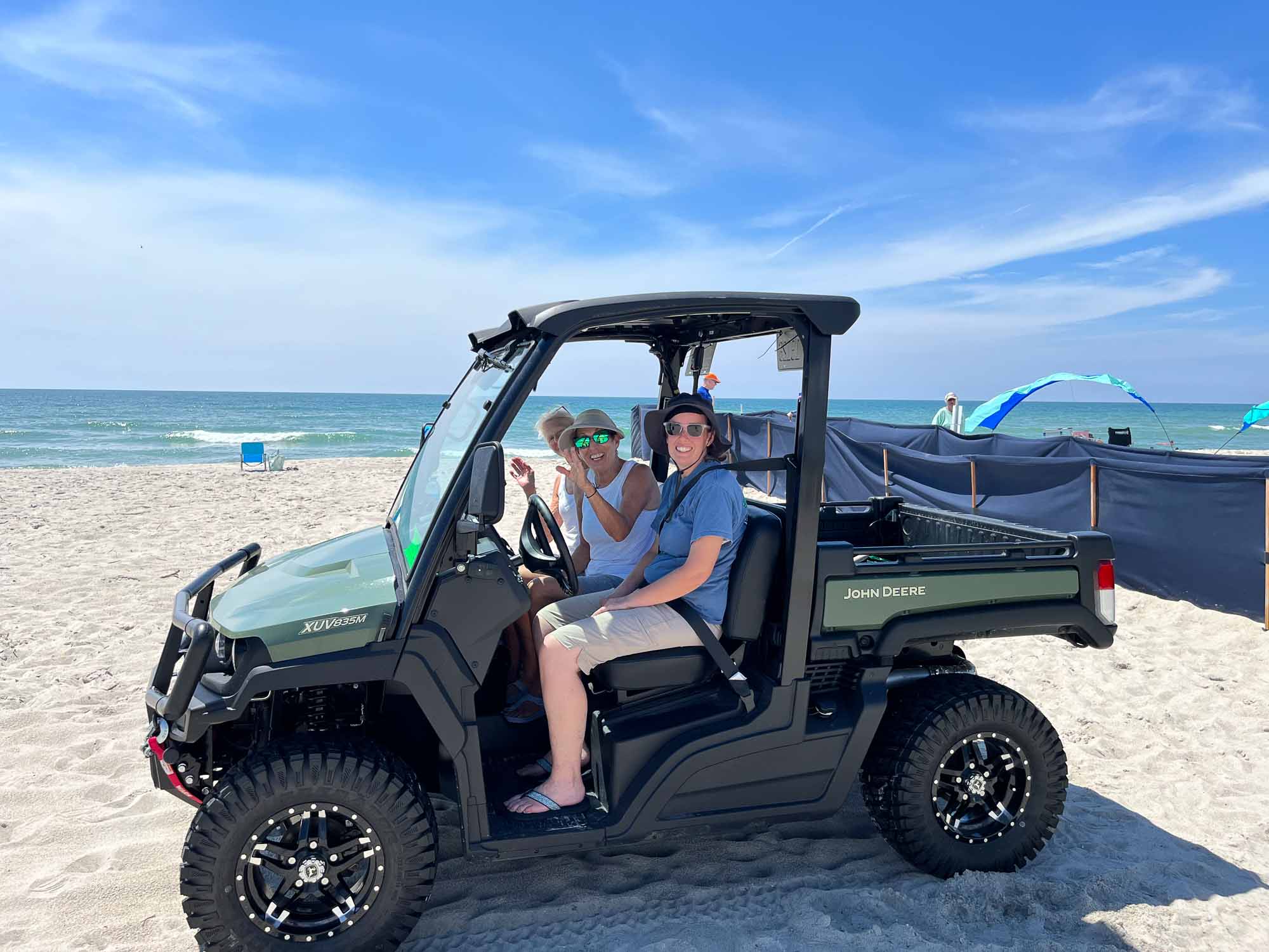 Three ABSTP volunteers in a UTV on the beach beside a trench with shade cloth.